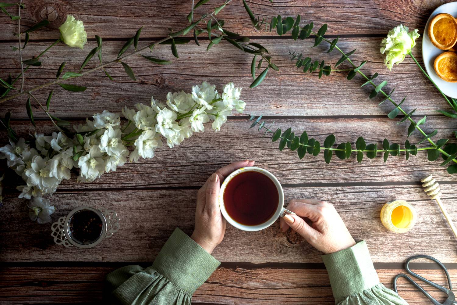 person enjoying tea with biscuits and honey at a wooden table adorned with flowers