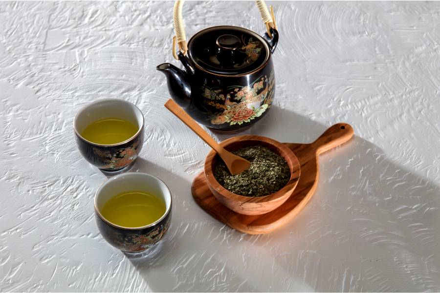 green tea set with two filled cups, a kettle, and crushed leaves