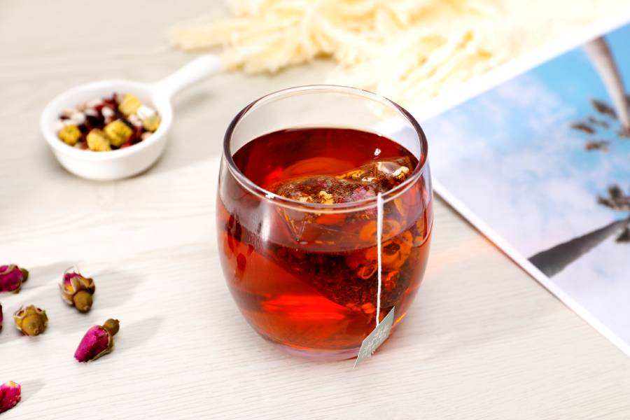 rooibos tea in a clear cup with rooibos tea leaves scattered on a table